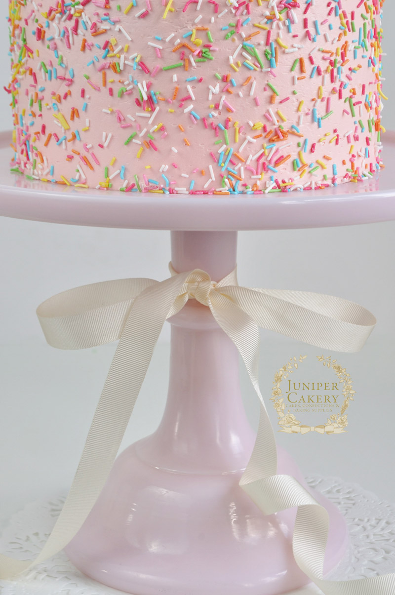 Rainbow sprinkles on a pink cake by Juniper Cakery