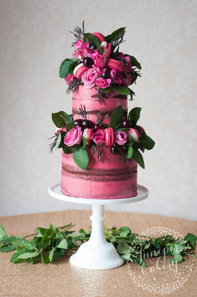 Pretty pink naked cake with cherries, macarons and roses by Juniper Cakery